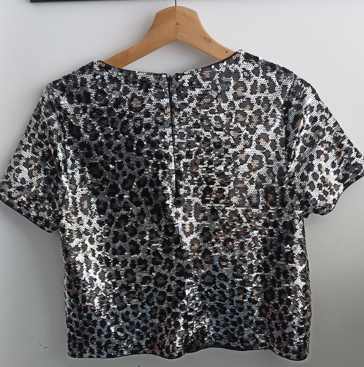Back of the Michael Kors animal-print sequined crop top on a hanger, showing the centre-back zip.