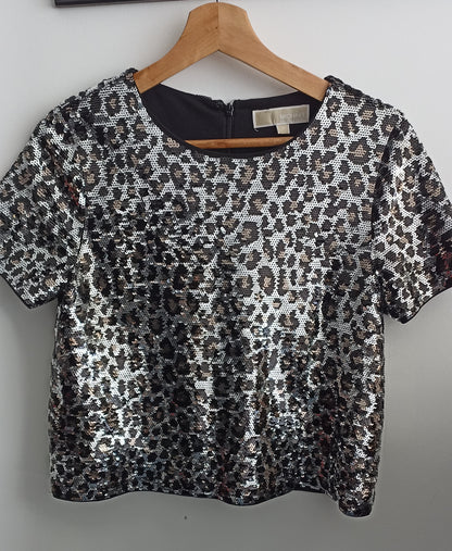 Front of the Michael Kors silver and black sequined crop top on a hanger, showing its round neckline and short sleeves.