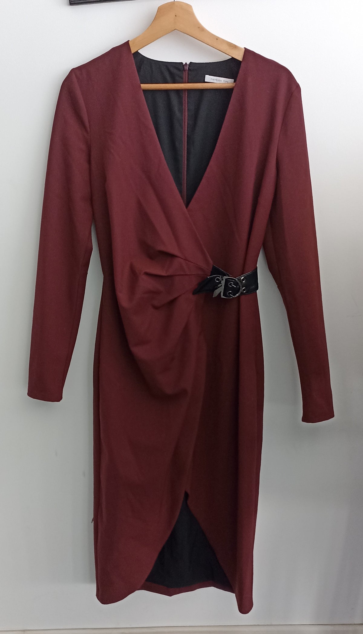 Front of the burgundy Patrizia Pepe dress on a hanger, showing the draped V-neck, black waist buckle and overlapping hem.
